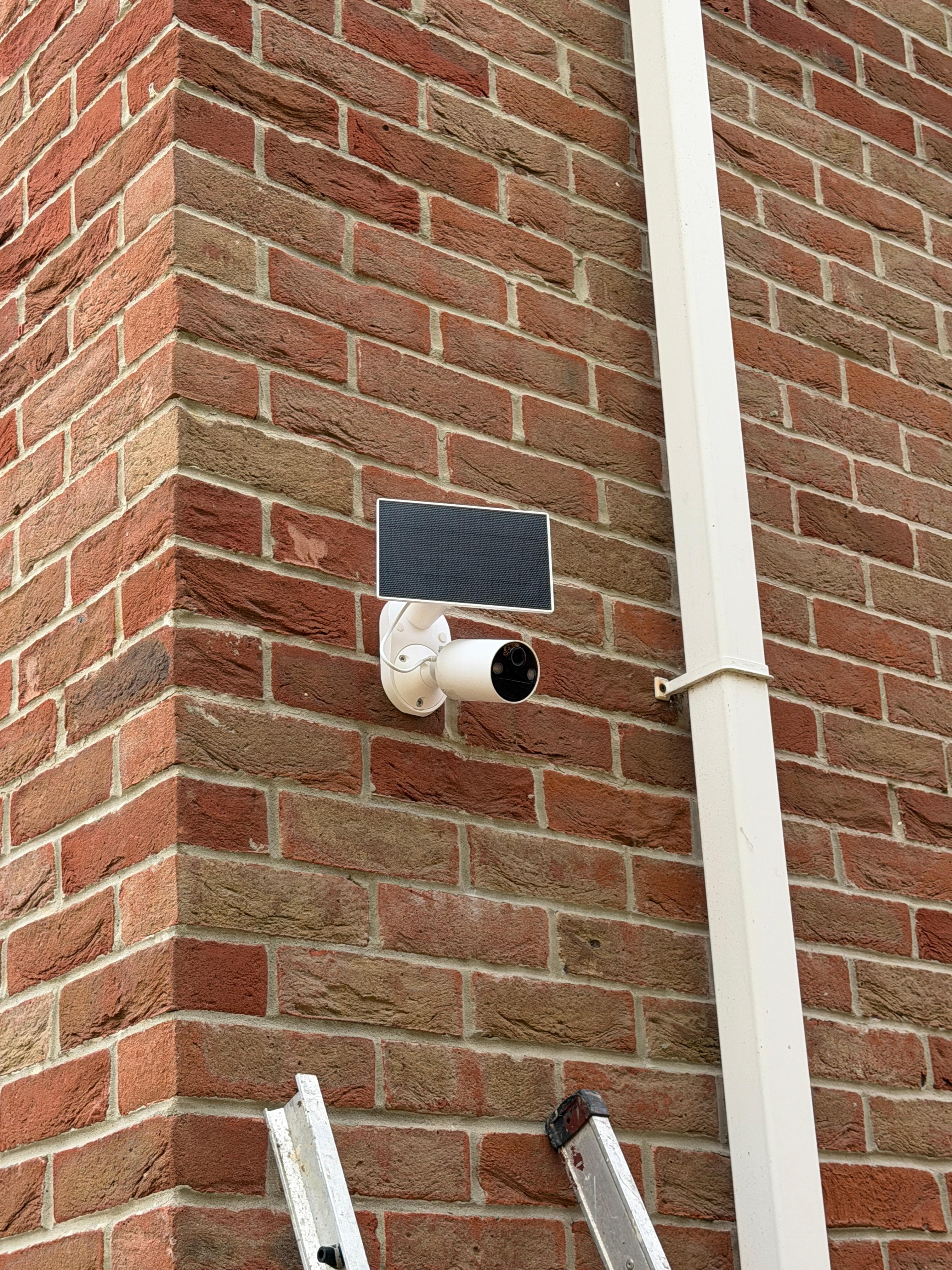 Solar security camera installed on a brick wall corner in natural daylight